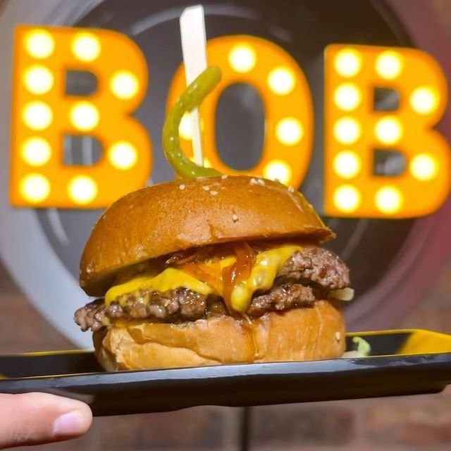 Delicious burger with melted cheese in front of illuminated "BOB" sign at Band of Burgers Fulham